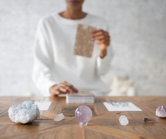 A person in focus arranging crystals and cards on a wooden table indoors.